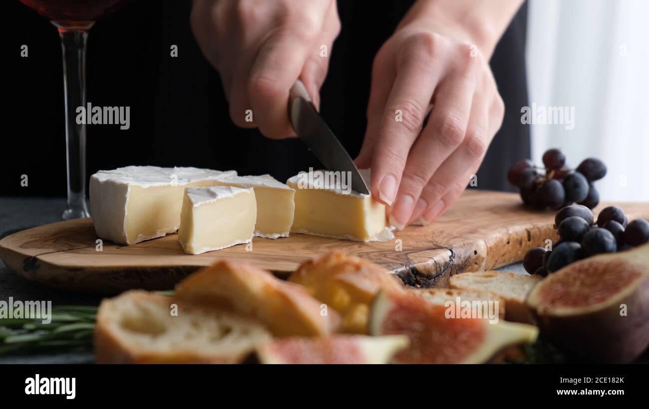 Slicing camembert cheese. Wine appetizer plate or cheese plate with figs, grapes, baguette and soft french camembert cheese Stock Photo