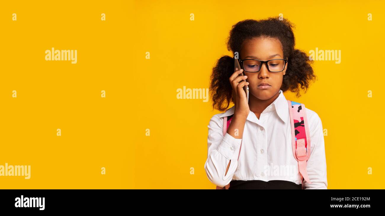 Offended Black Schoolgirl Calling To Helpline Standing Over Yellow Background Stock Photo