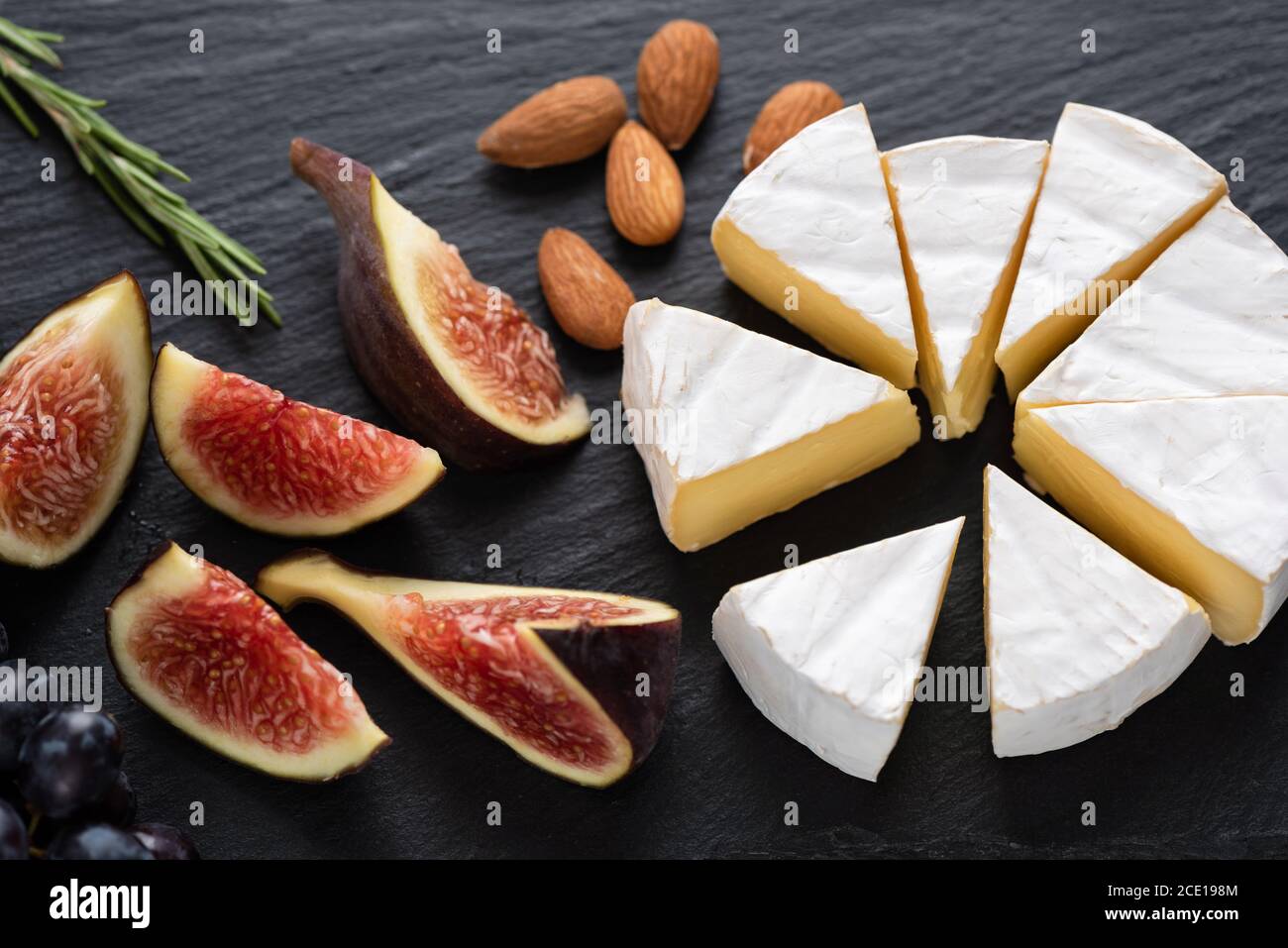 Camembert cheese with figs and almonds on black slate. Cheese appetizer plate Stock Photo