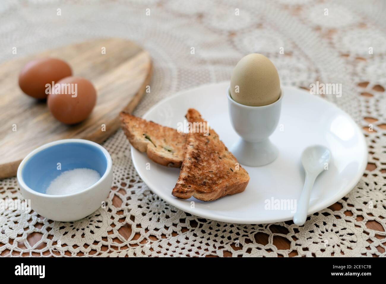 Tasty boiled egg in a cup with crunchy toasted bread for breakfast. Healthy meal on the kitchen table. Stock Photo