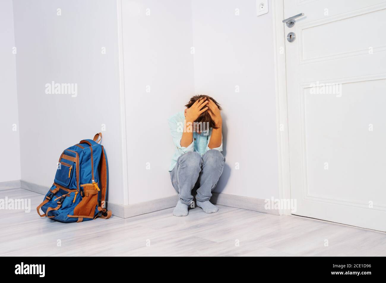 Portrait of a sad stressed boy bullied in school cry sitting in the corner with son rucksack Stock Photo