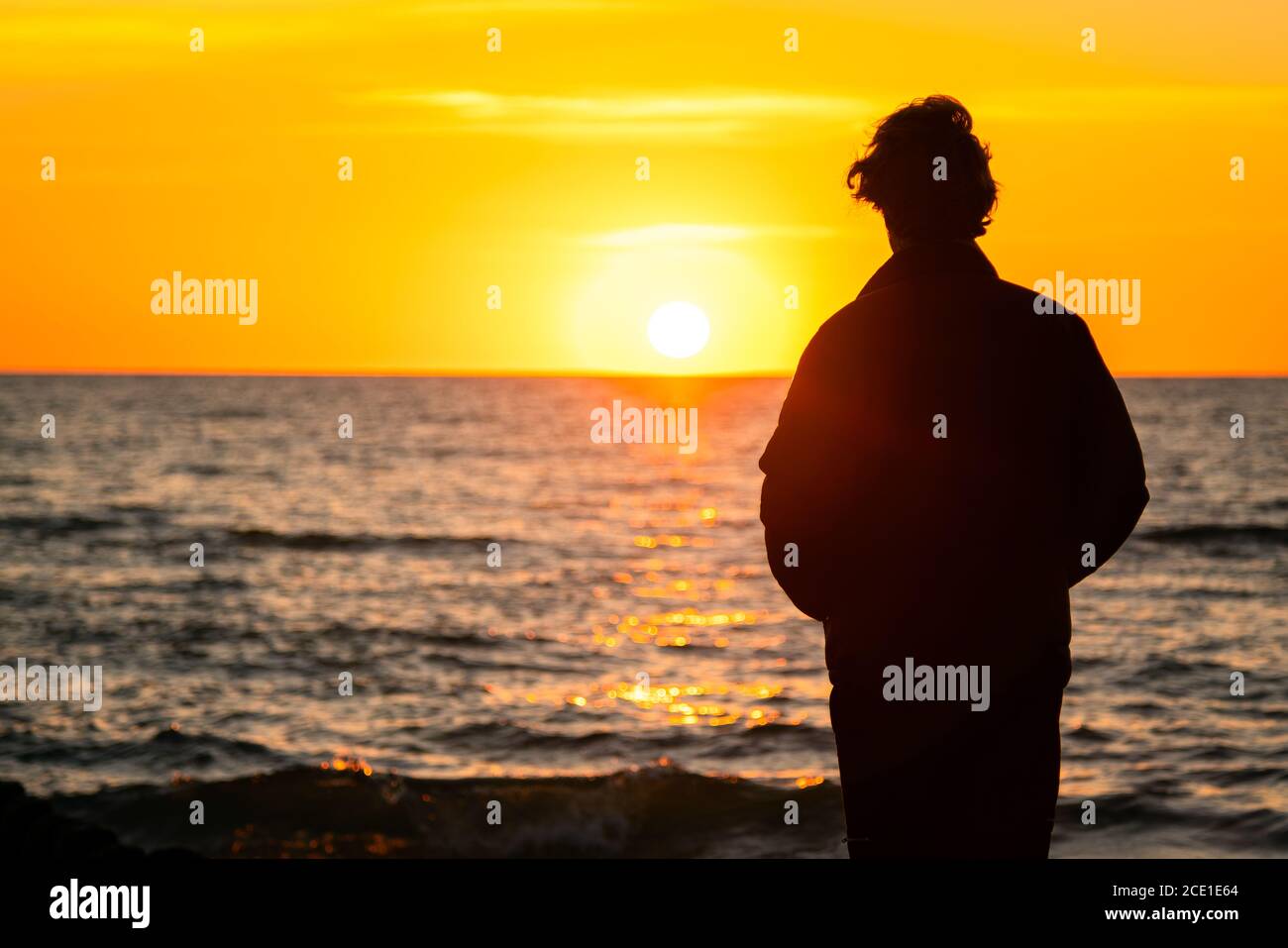 Dark silhouette of a man standing by the sea at golden sunset. Lonely ...