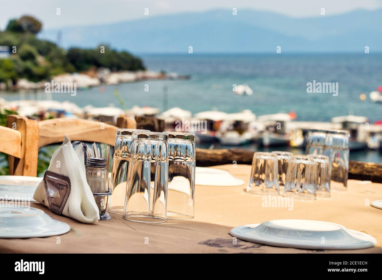 Glasses and plates on a wooden table of a greek tavern over the view of the port of Amaliapoli, Greece Stock Photo