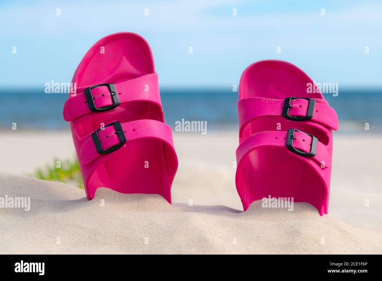 Pink sandals at the beach on a beautiful sunny day. Slippers in the sand by the sea. Flip flops at the shore by the ocean. Stock Photo