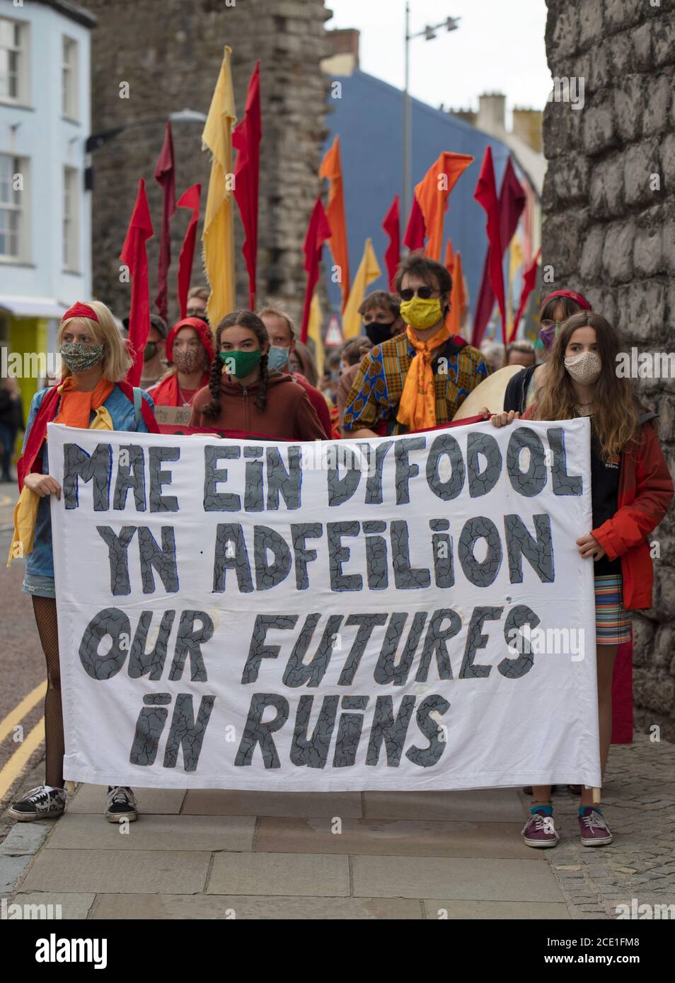 Caernarfon Castle, Wales, UK. 30 August 2020, Extinction Rebellion Protestors and Red Rebel Brigade take over Caernarfon Castle to protest about climate change and global warming. Children's shoes signify that it is the children that will suffer in the future. Protestors hold a banner stating our future in ruins carrying red, orange and yellow flags Credit: Denise Laura Baker/Alamy Live News Stock Photo