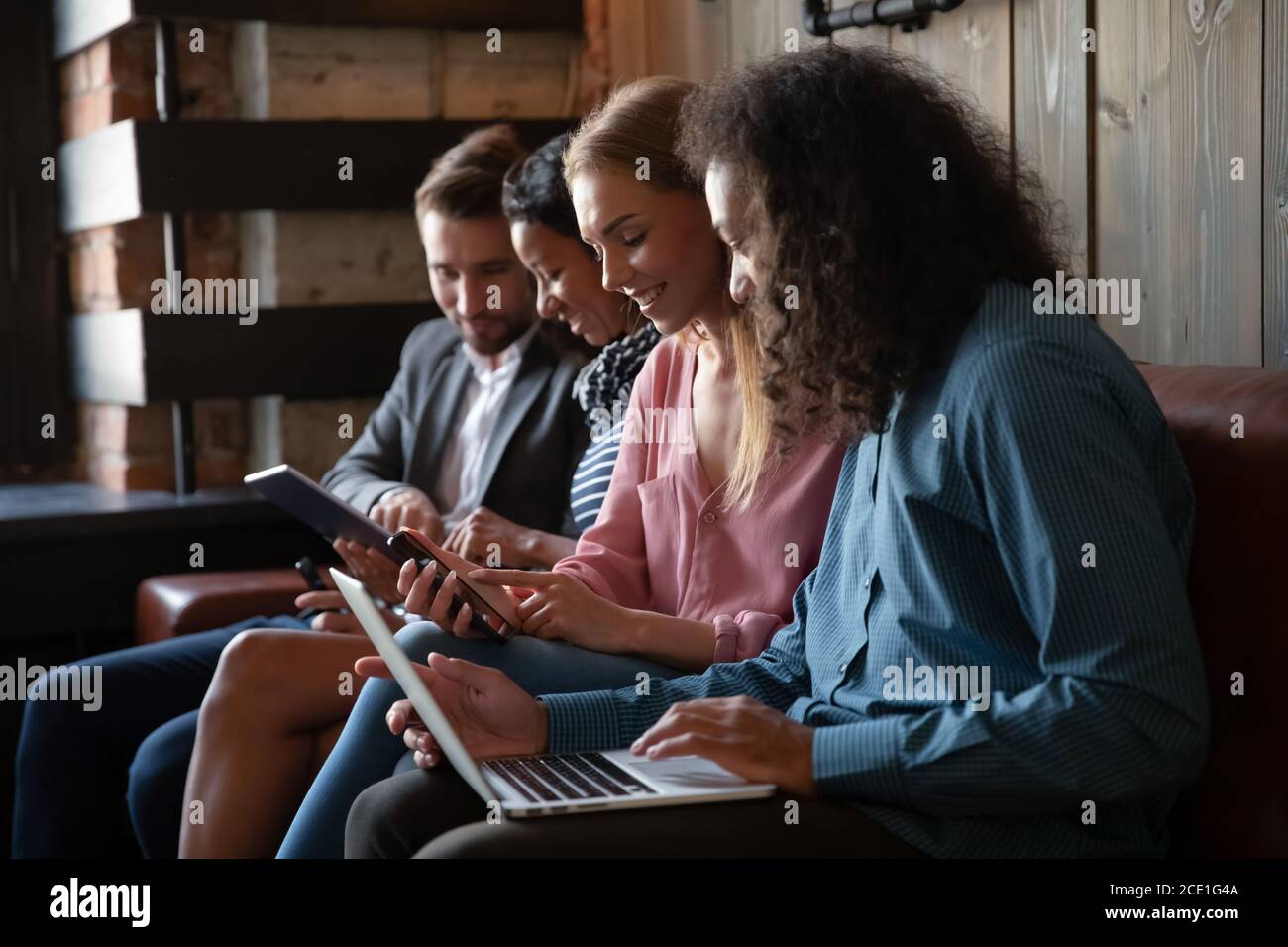 Diverse friends using gadgets together, sitting on couch in row Stock Photo
