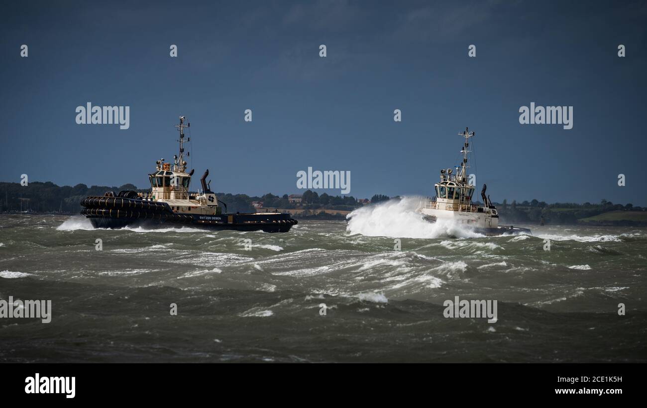 Tugs in stormy seas - two tugs navigate through stormy water to meet a ship entering Felixstowe Port UK Stock Photo