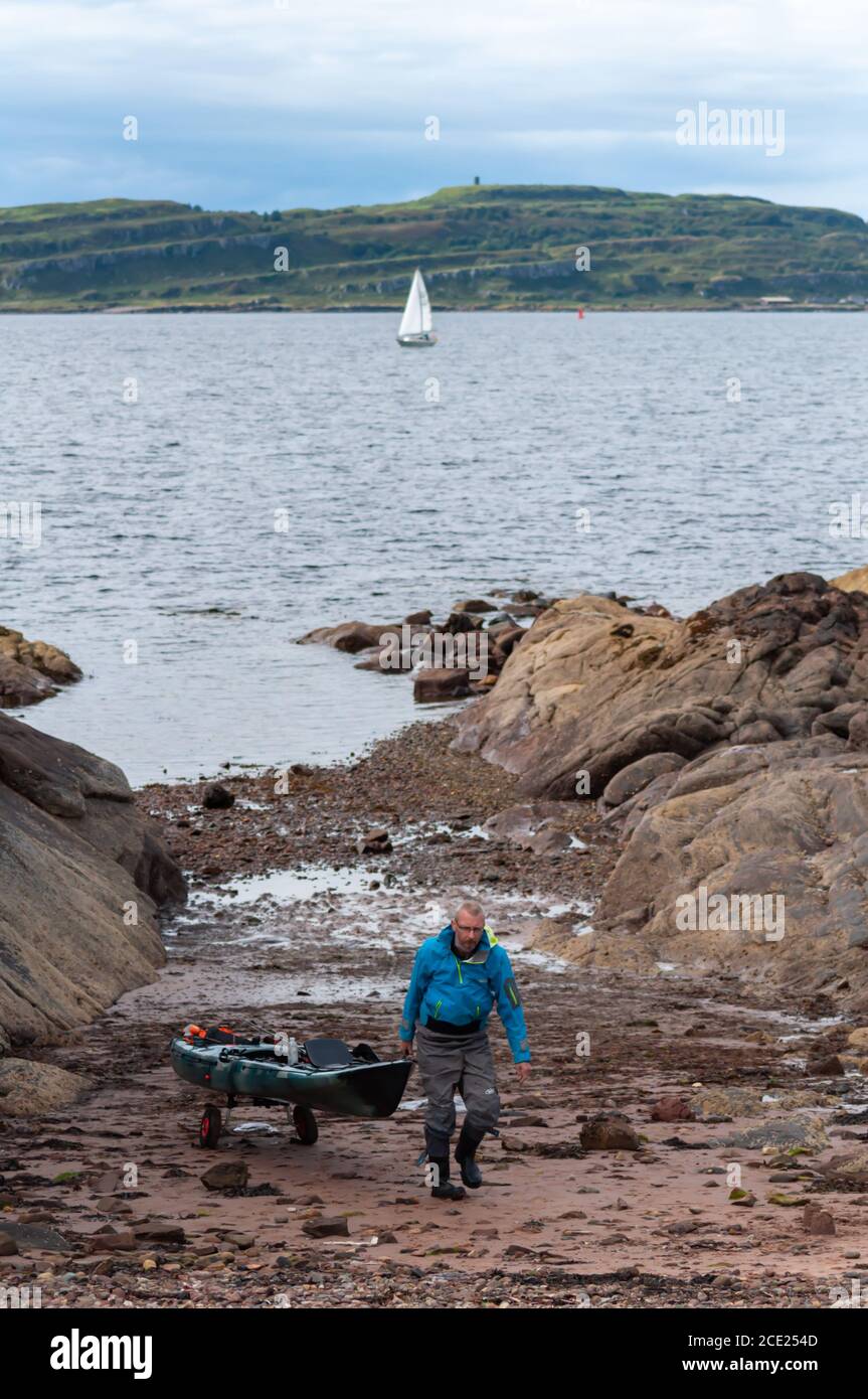 Portencross, Scotland, UK. 30th August 2020. UK Weather: A fisherman pulls his boat up the shore with the Isle of Little Cumbrae in the background. Credit: Skully/Alamy Live News Stock Photo