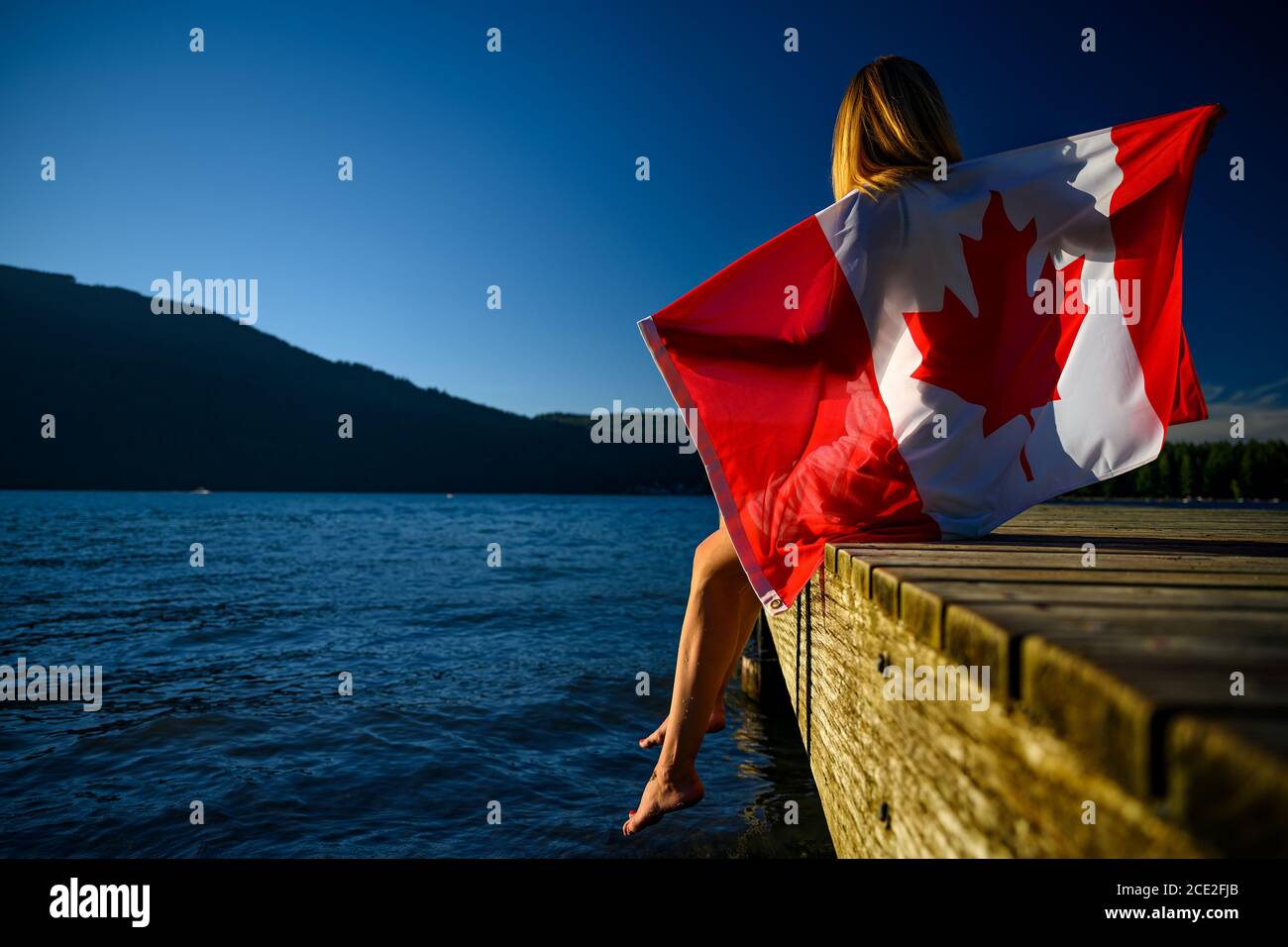 Summer scene of the Cultus Lake with a patriot woman in the foreground holding up a Canadian flag. Chilliwack, British Columbia, Canada Stock Photo