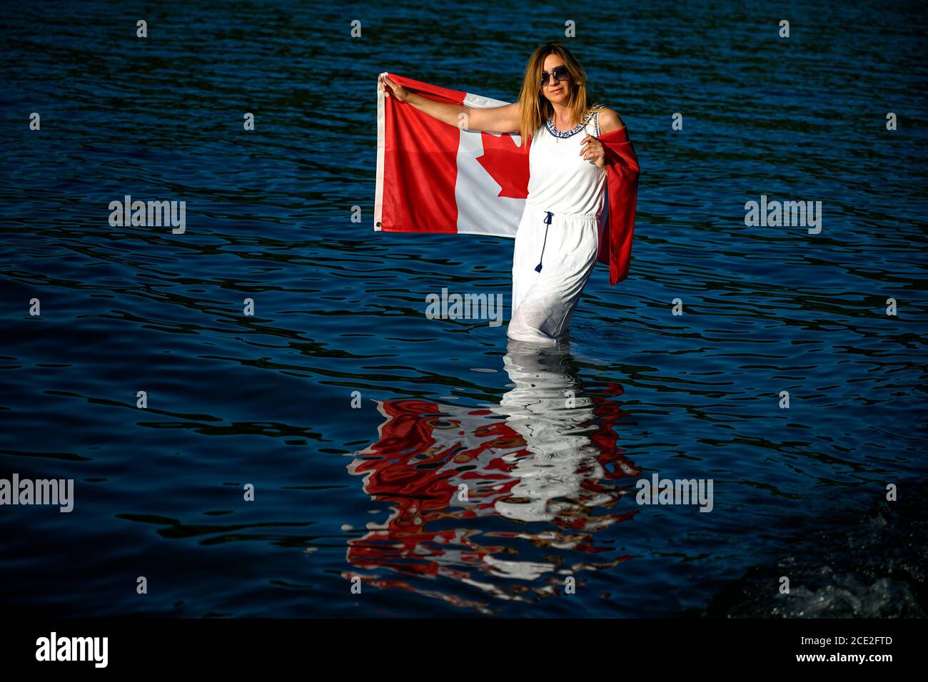 Summer scene of the Cultus Lake with a patriot woman in the foreground holding up a Canadian flag. Chilliwack, British Columbia, Canada Stock Photo