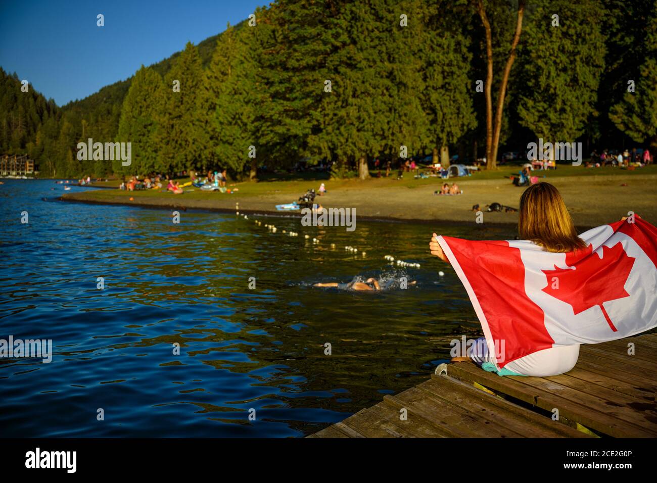 Summer scene of the Cultus Lake with a patriot woman in the foreground holding up a Canadian flag. Chilliwack, British Columbia, Canada Stock Photo