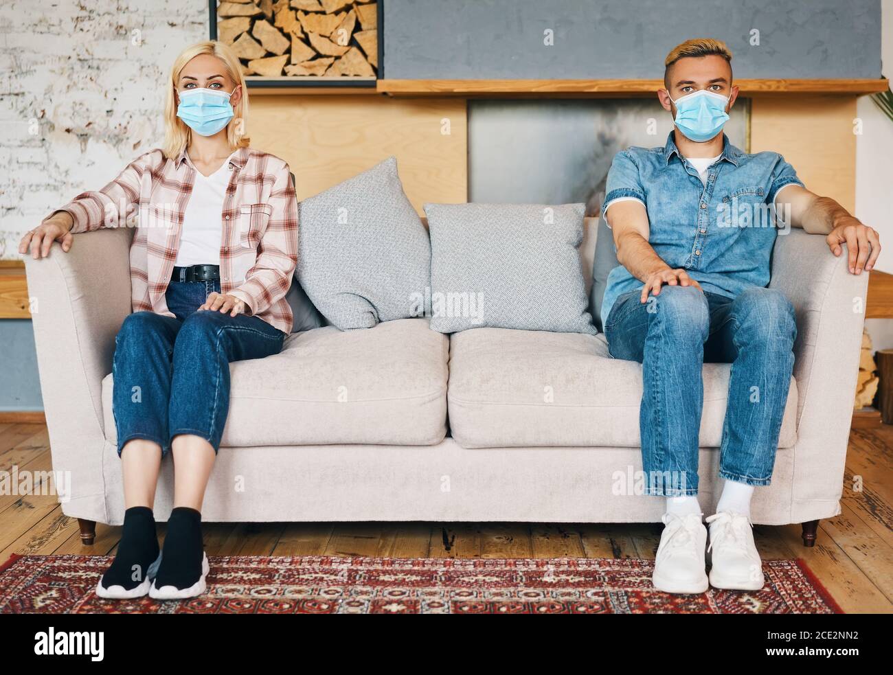 Man and woman in facemask sitting on sofa at home Stock Photo