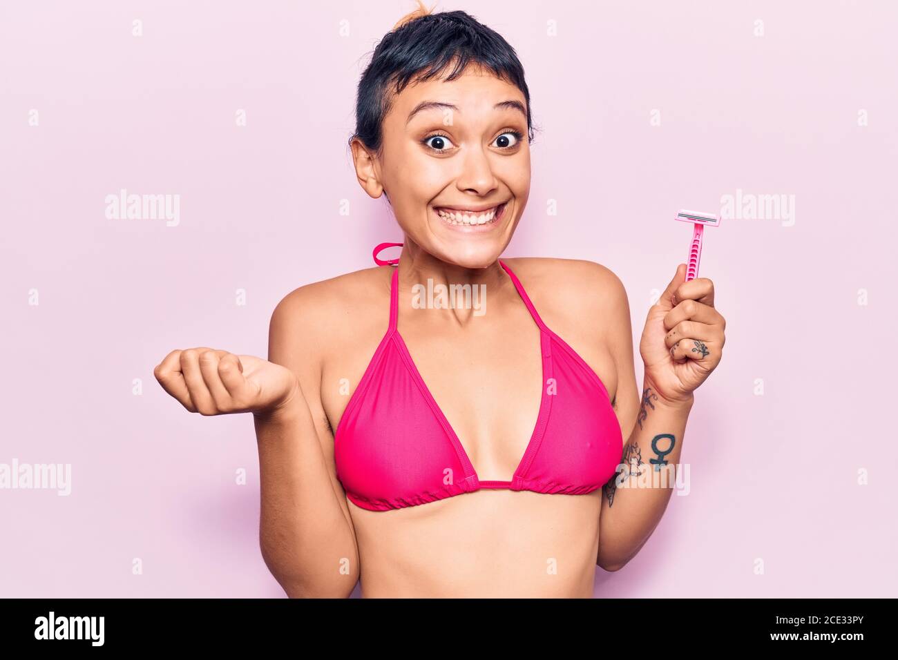 Unshaven young woman smiling cheerfully while wearing a bra and