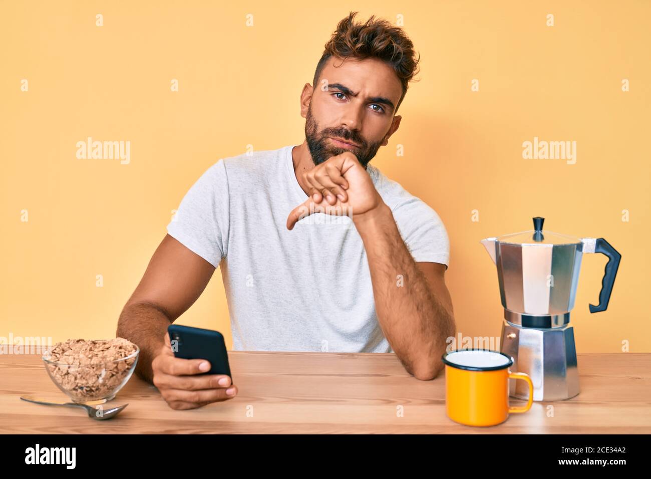 Young hispanic man sitting on the table having breakfast and using ...