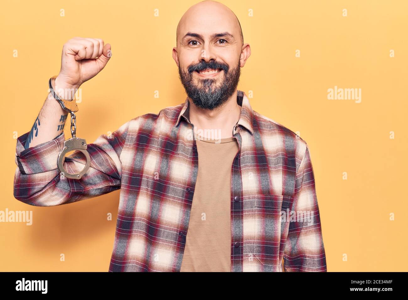 Young handsome man wearing prisoner handcuffs looking positive and happy standing and smiling with a confident smile showing teeth Stock Photo