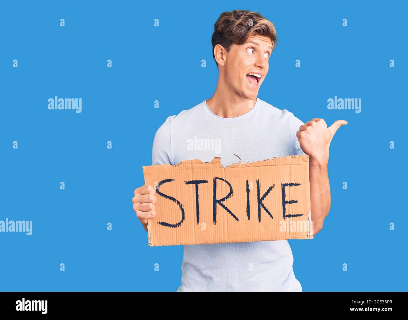 Young handsome man holding strike banner cardboard pointing thumb up to ...