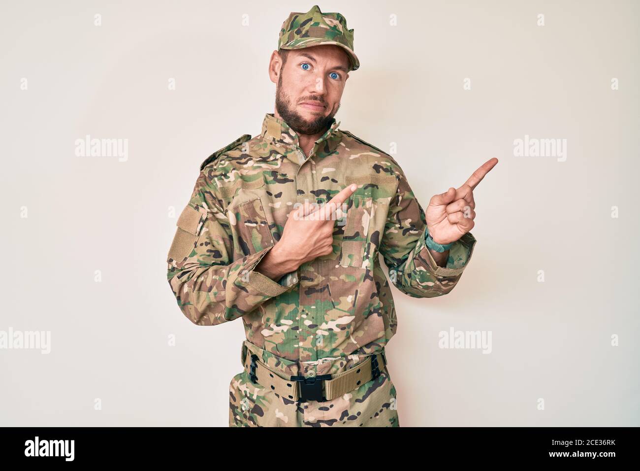 Scared Army Young caucasian man wearing camouflage army uniform pointing aside ...