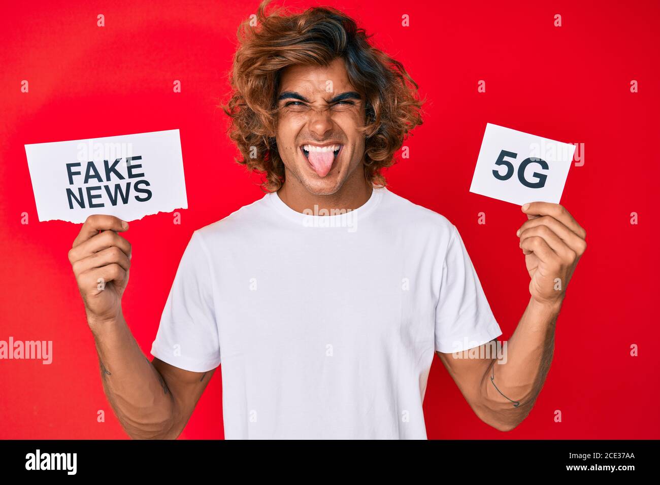 Young hispanic man holding fake news and 5g banner sticking tongue out  happy with funny expression Stock Photo - Alamy
