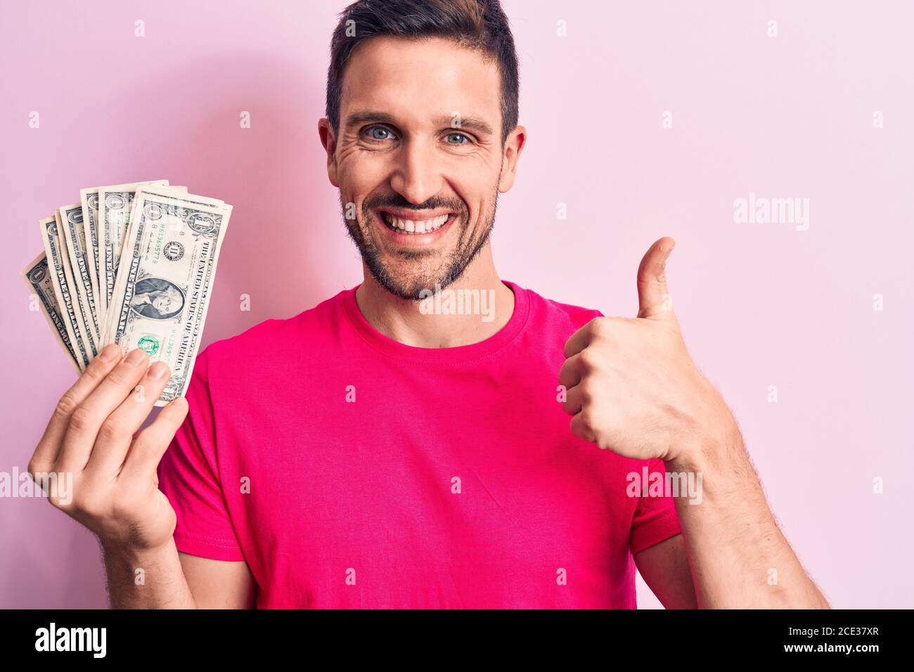 Young handsome man holding bunch of dollars banknotes over isolated ...