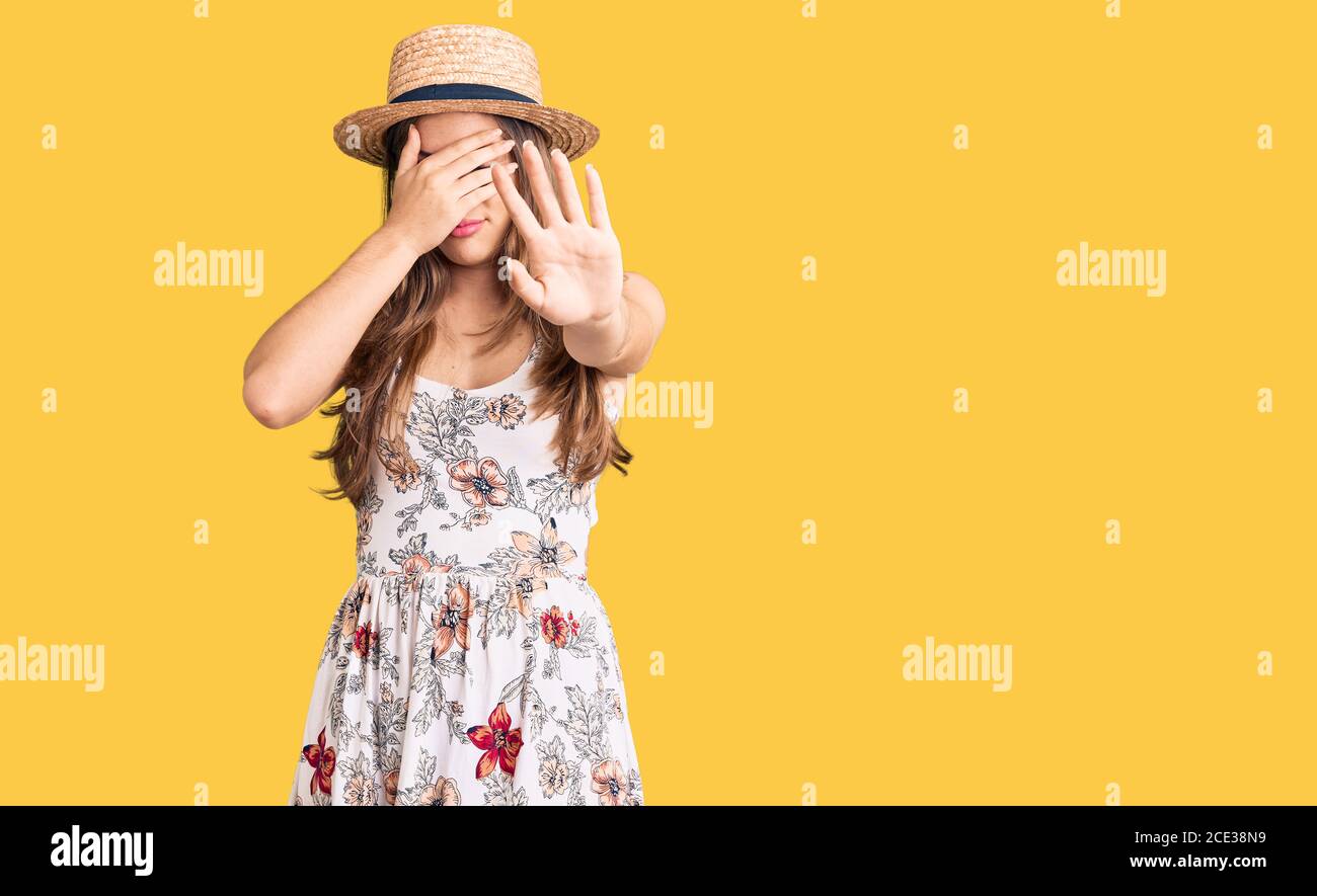 Beautiful caucasian young woman wearing summer hat covering eyes with hands and doing stop gesture with sad and fear expression. embarrassed and negat Stock Photo