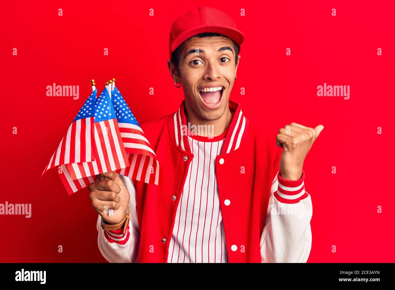 Young african amercian man wearing baseball uniform holding america flags pointing thumb up to the side smiling happy with open mouth Stock Photo