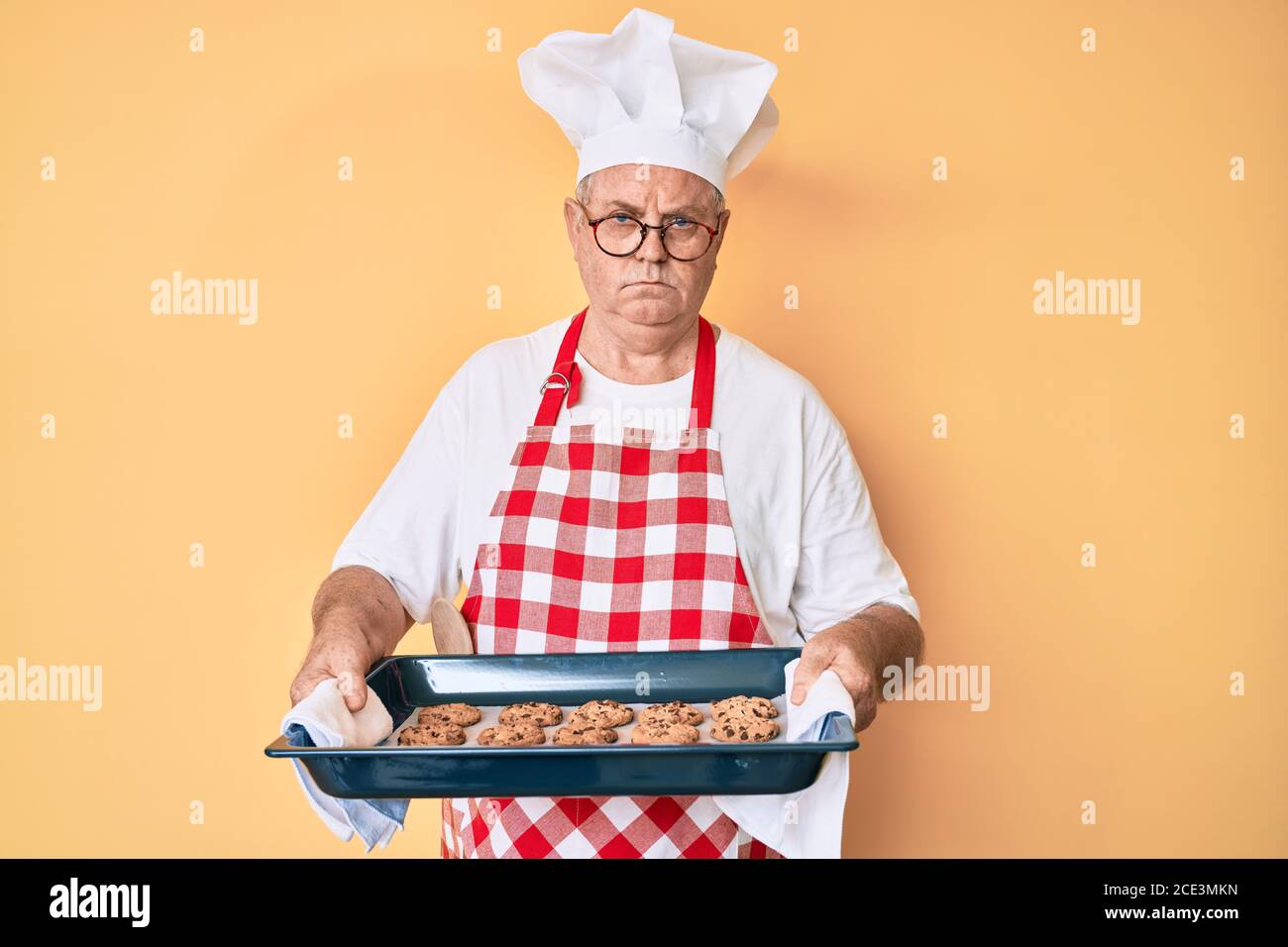Senior grey-haired man wearing baker uniform holding homemade cookies ...