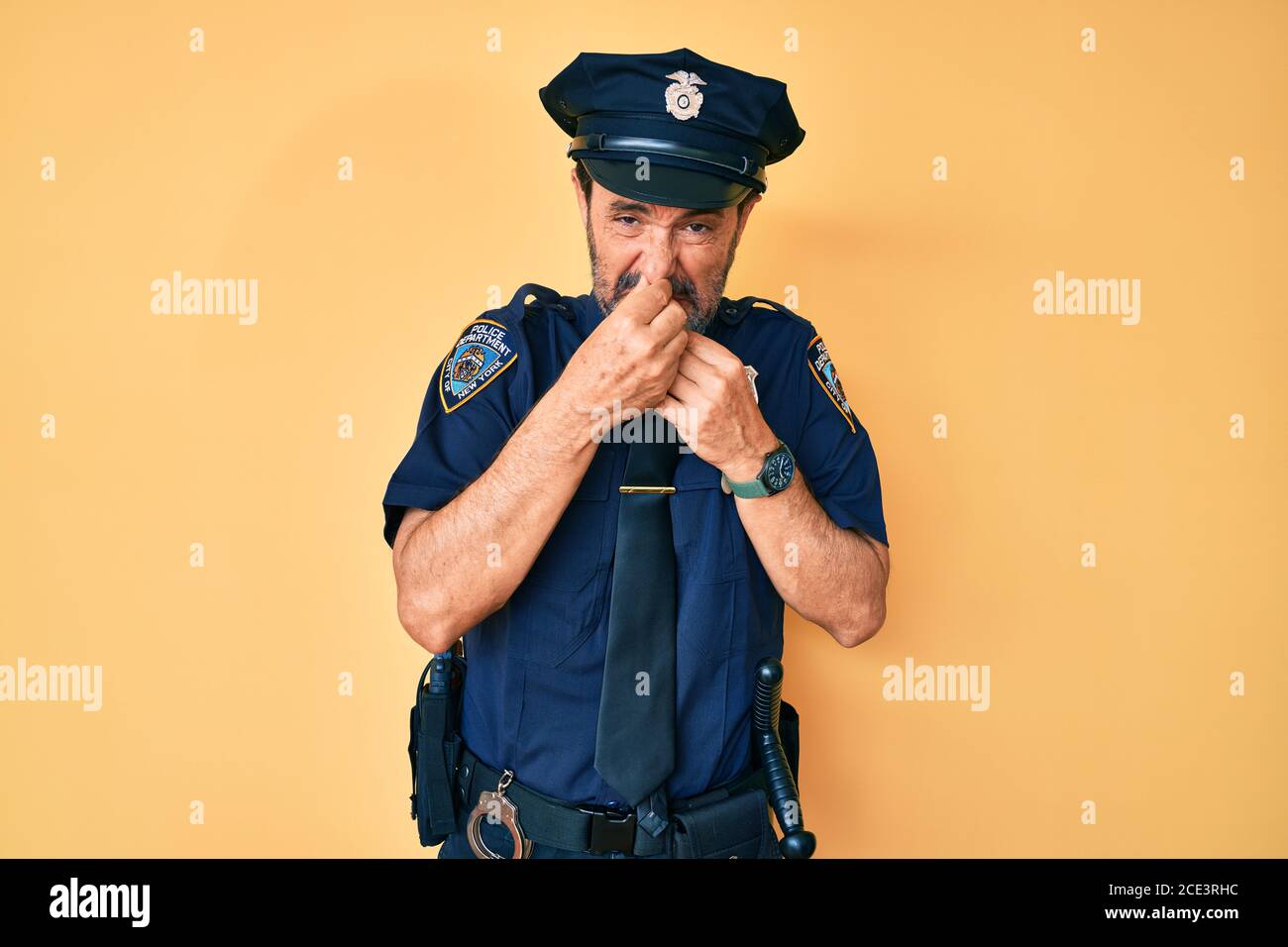 Middle age hispanic man wearing police uniform smelling something ...