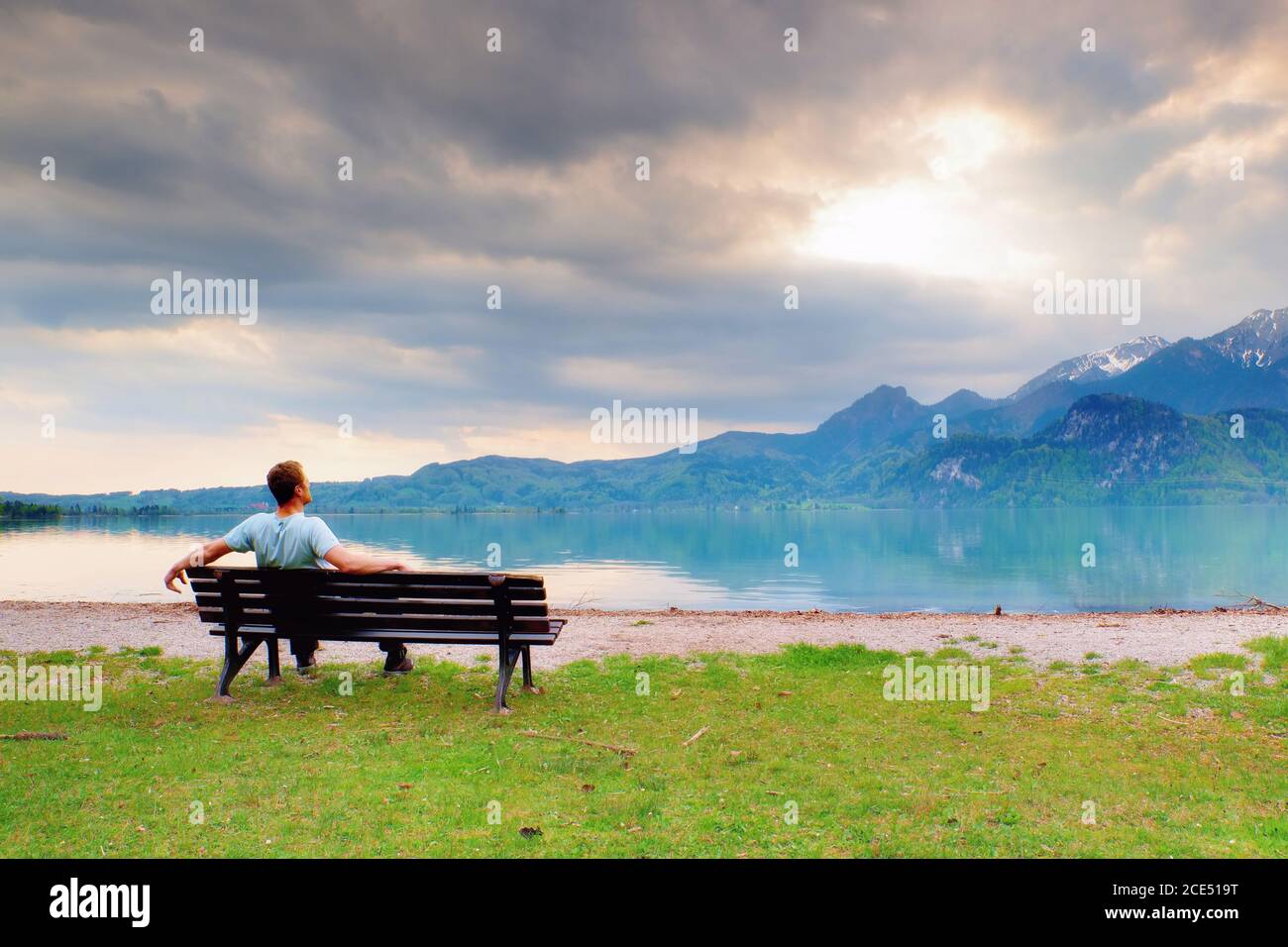 Alone  man sits on bench beside an azure mountain lake. Man relax Stock Photo