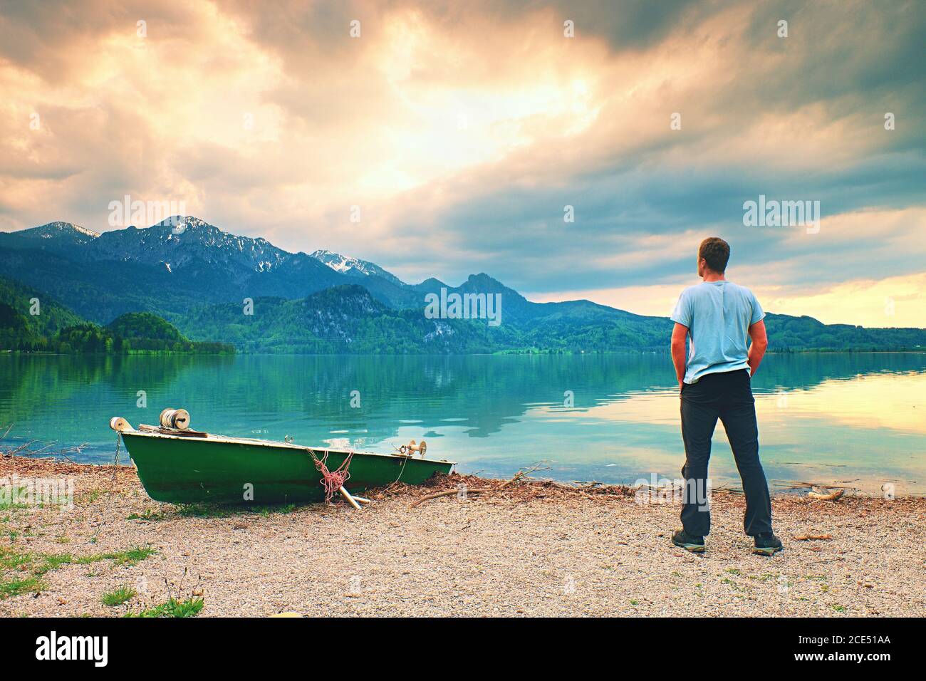 Adult man in blue shirt walk at old fishing paddle boat at mountains lake coast. Stock Photo