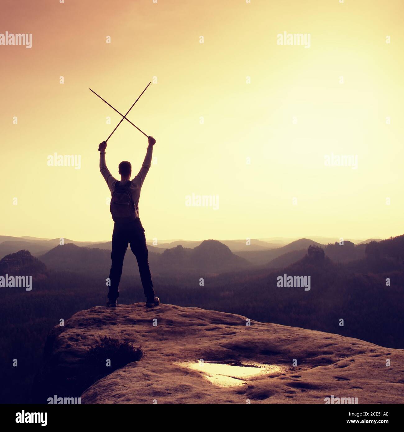 Happy hiker with x crossed poles above head.  Foggy  mountain valley bellow. Tall tourist enthusiast Stock Photo