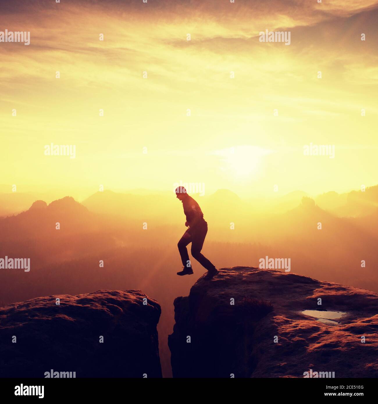 Man in black jumping between peaks. Dreamy daybreak Stock Photo