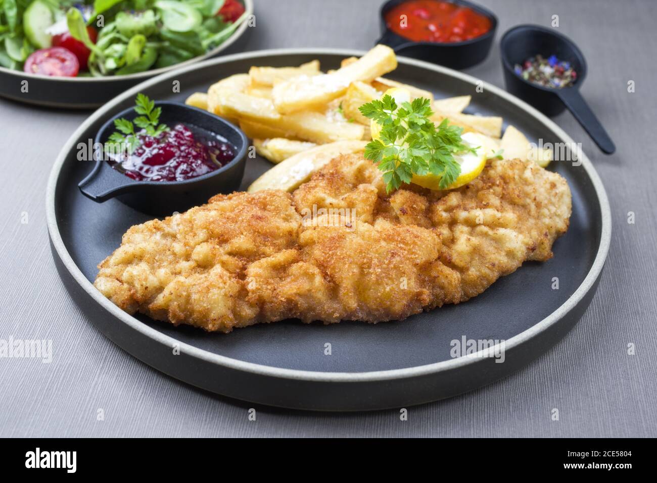 Fried Wiener schnitzel from veal topside with French fries and lettuce as closeup modern design