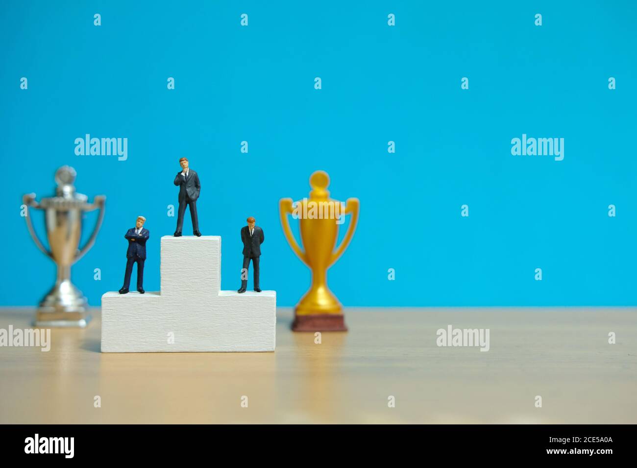 Miniature business concept - three businessman standing on winner podium with golden and silver trophy Stock Photo
