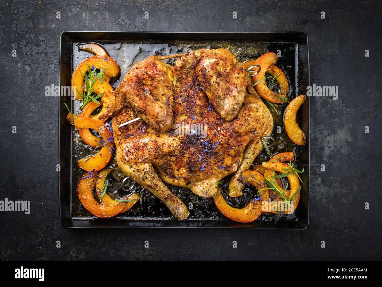Barbecue spatchcocked chicken al mattone chili with pumpkin and herbs as top view on an old metal tray Stock Photo