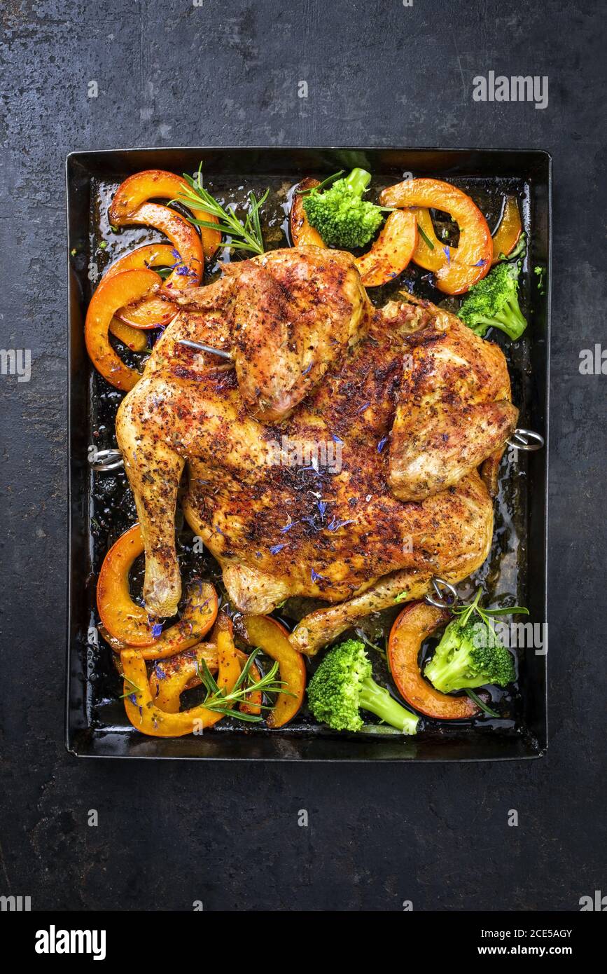 Barbecue spatchcocked chicken al mattone chili with pumpkin and broccoli as top view on an old metal tray Stock Photo