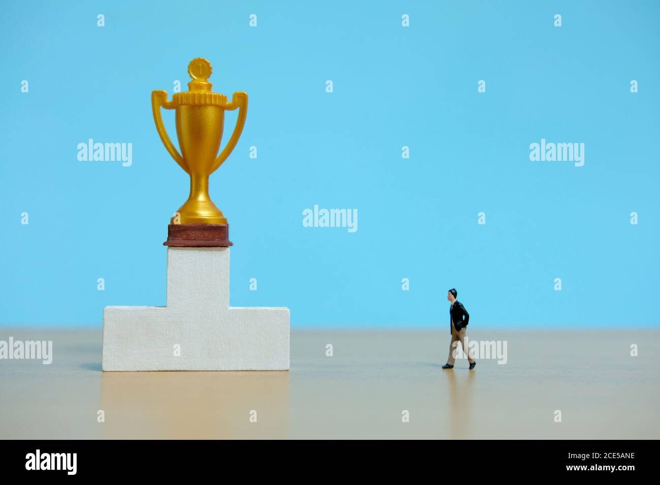 Miniature business concept - businessman walking toward golden trophy above white podium Stock Photo