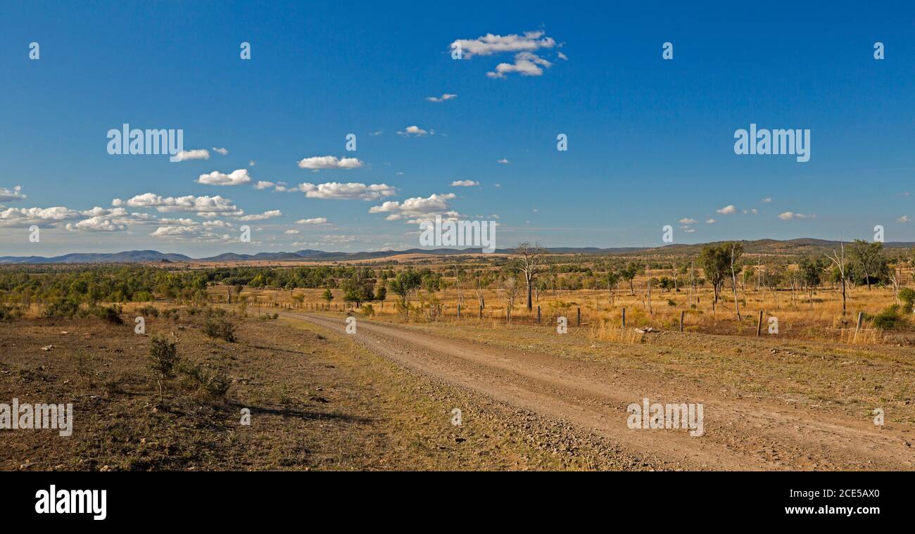 Panoramic view of arid Australian outback landscape during drought with red gravel road spearing across plains to distant ranges under blue sky Stock Photo