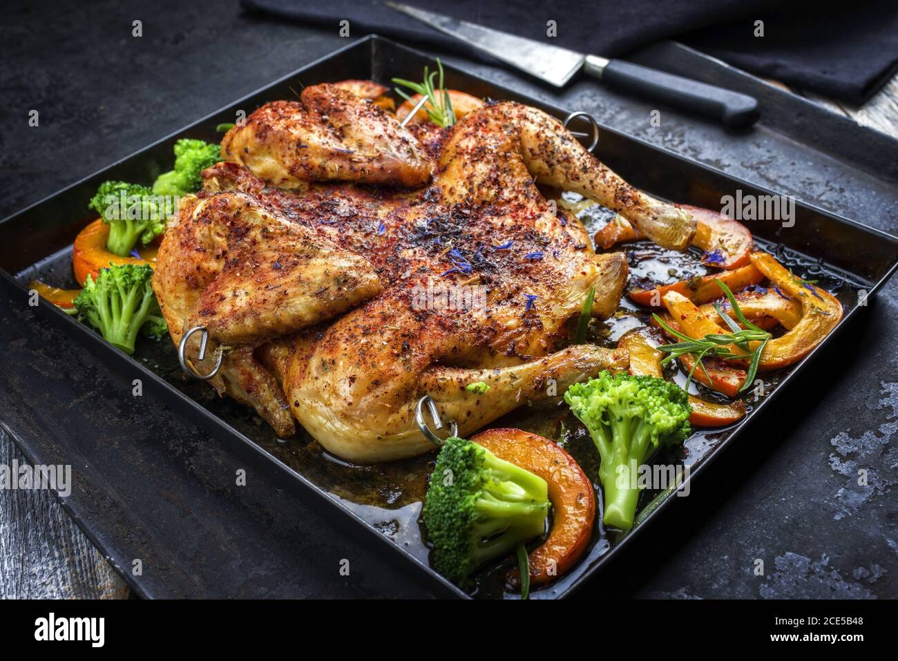 Barbecue spatchcocked chicken al mattone chili with pumpkin and broccoli as closeup on an old metal tray Stock Photo