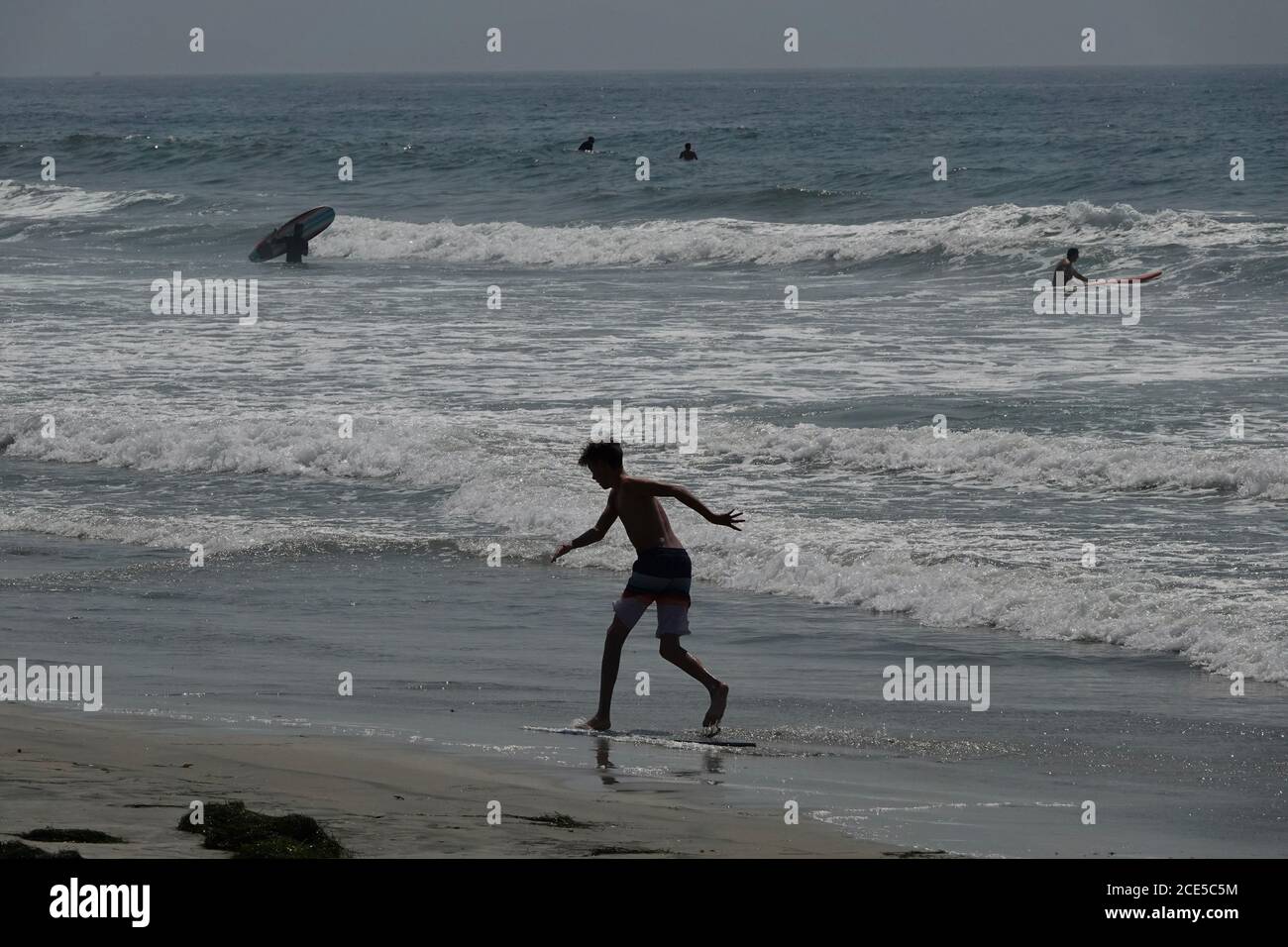 A silhouette of a boy skim boarding near the oceans edge on the beach. Stock Photo