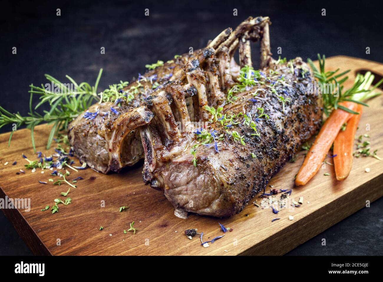 Barbecue rack of lamb with carrot and herbs offered as closeup on a modern design wooden board