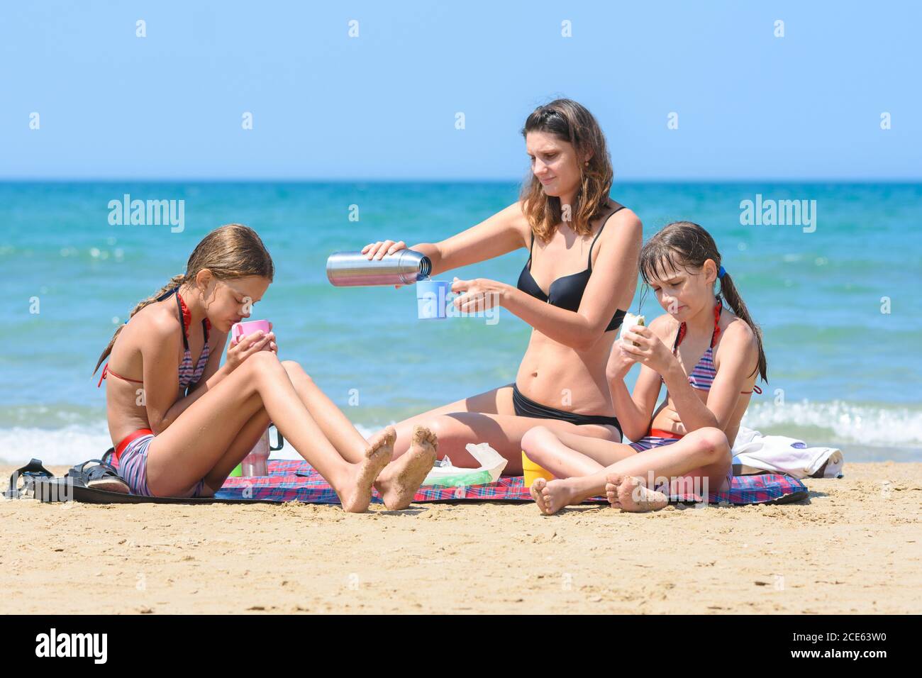 Mom pours tea from a thermos, having lunch on the sea beach Stock Photo