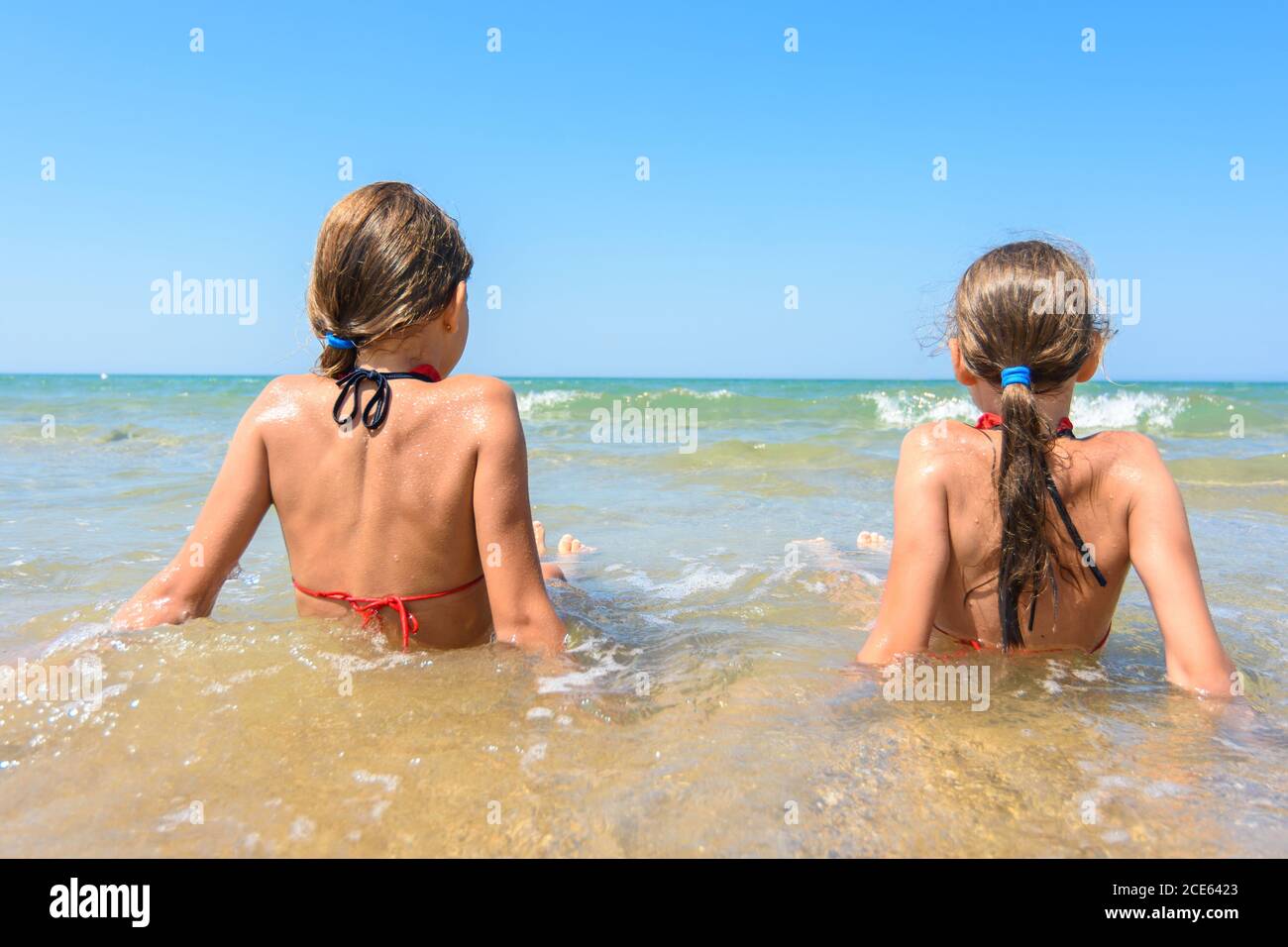 Children sit in the water on the coast and look into the distance Stock Photo