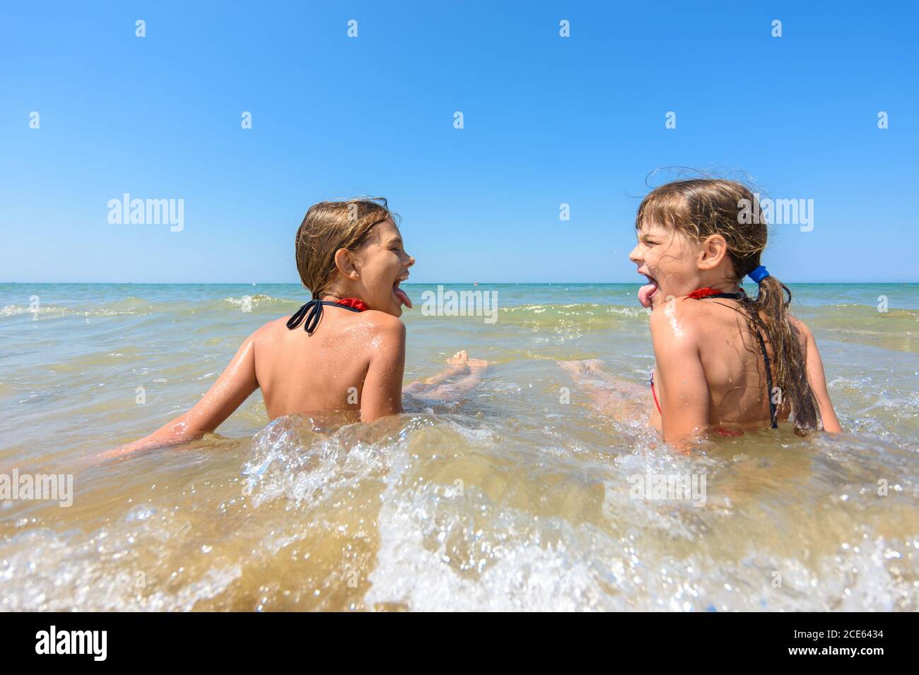 Children sit together in shallow water and show each other tongue Stock Photo