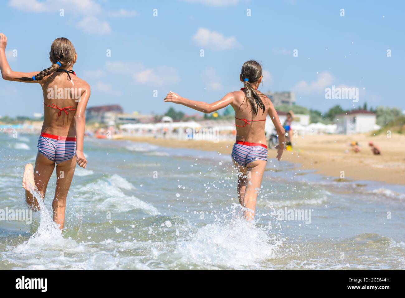 Two girls joyfully run along the sea on a warm summer day, rear view Stock Photo