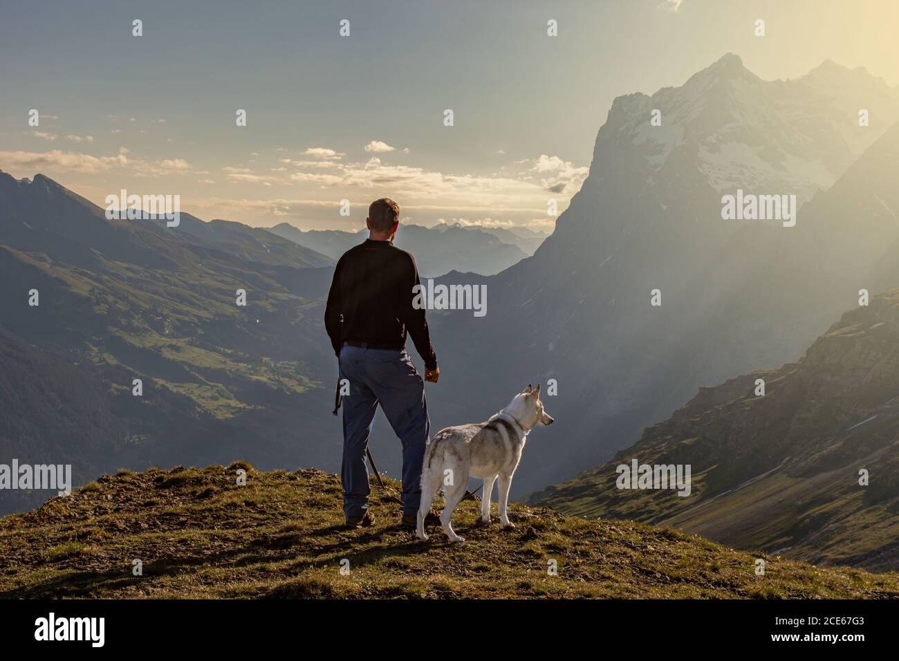 A man enjoying with his husky dog the beautiful view to the valley. // Ein Mann geniesst mit seinem Husky die schöne Aussicht in das Tal. Stock Photo