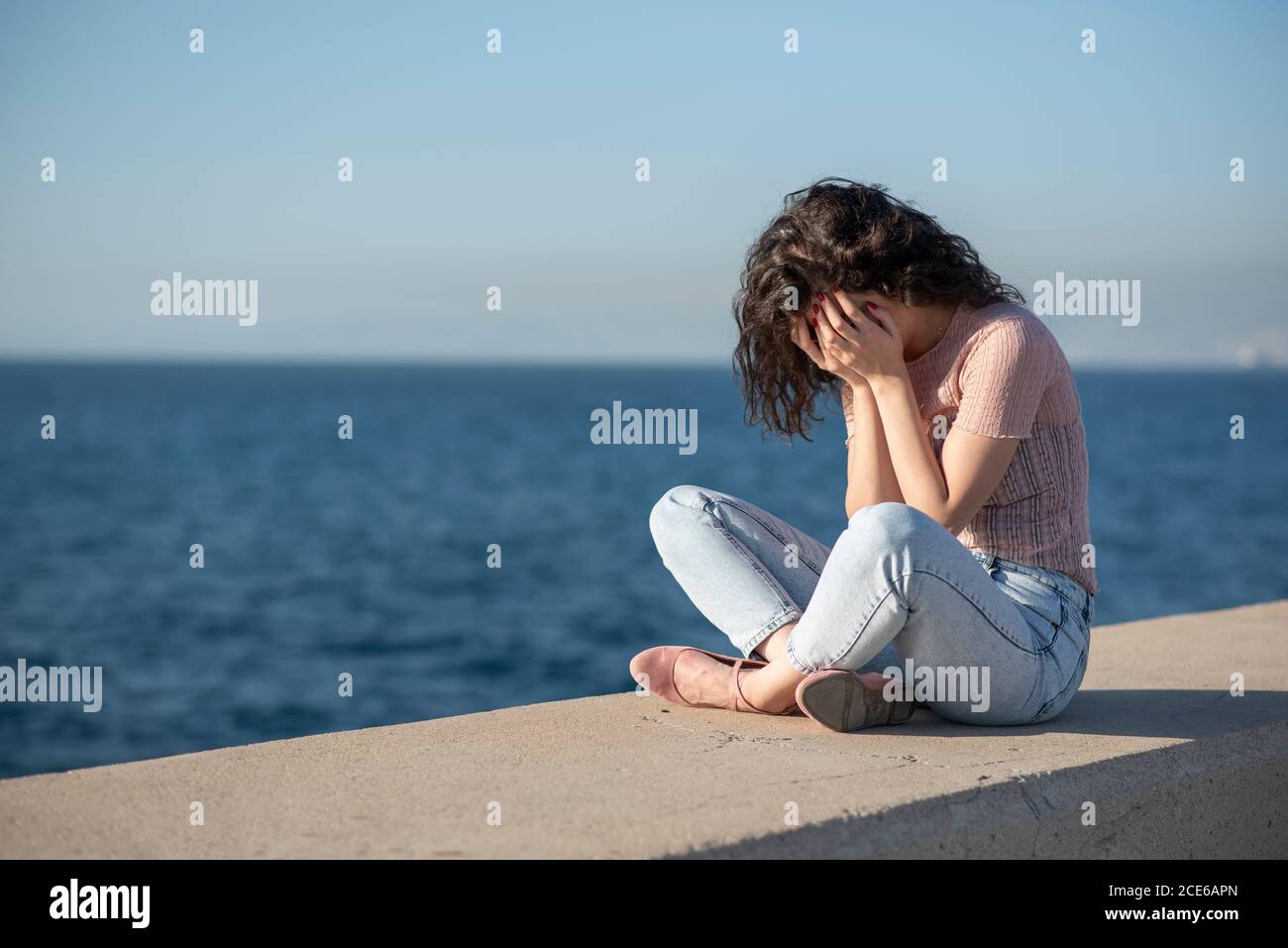 Stressed woman head in hands crying by the sea Stock Photo