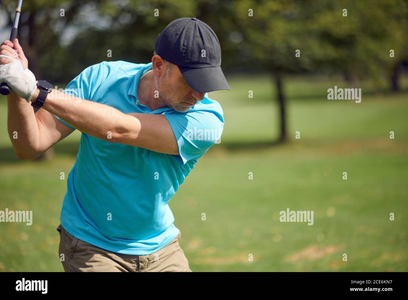 Male golfer swinging at the ball with a driver as he takes his shot on a golf course in a closeup upper body view in a healthy active lifestyle concep Stock Photo