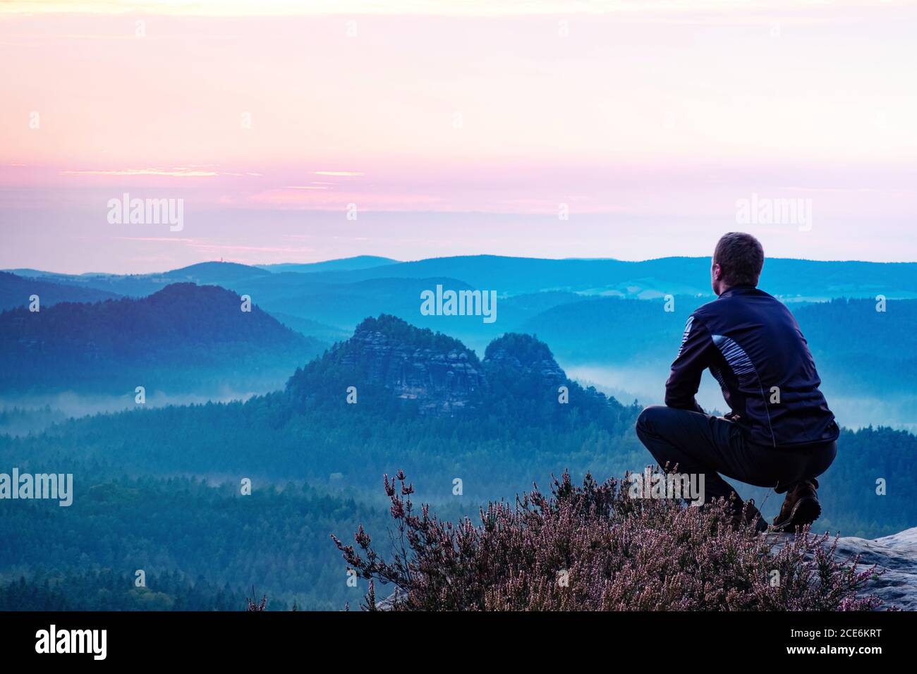 Calm man sitting on top of mountain enjoying view Stock Photo