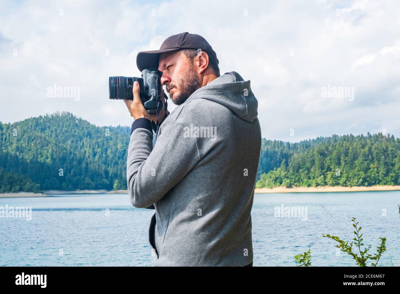 Photographer man in hoodie walking around lake with DSLR camera and shooting nature, half body portrait, landscape photography concept Stock Photo