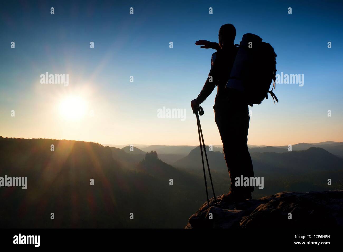 Sharp silhouette of a tall man on the top of the mountain with sun in the frame. Tourist guide in mountains Stock Photo